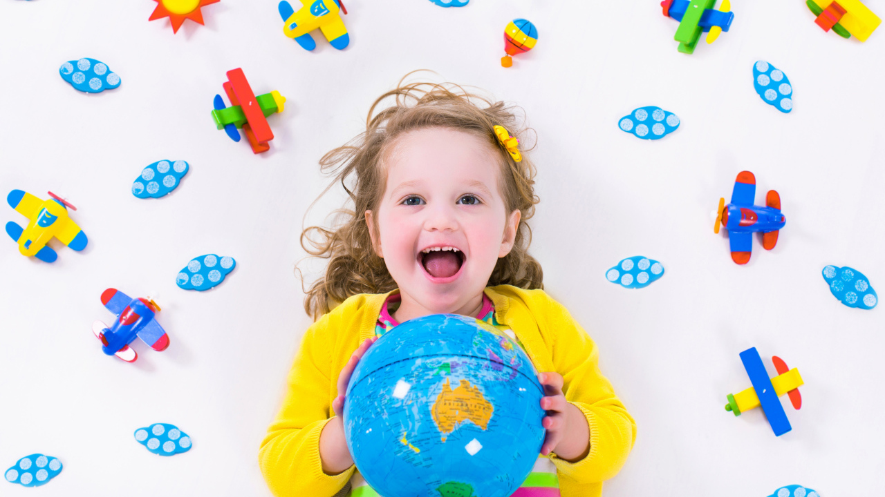 Маленькая веселая девочка с глобусом в руках 