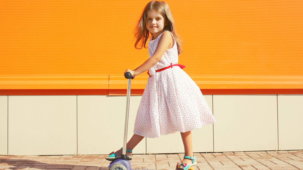 Маленькая девочка в платье на самокате 