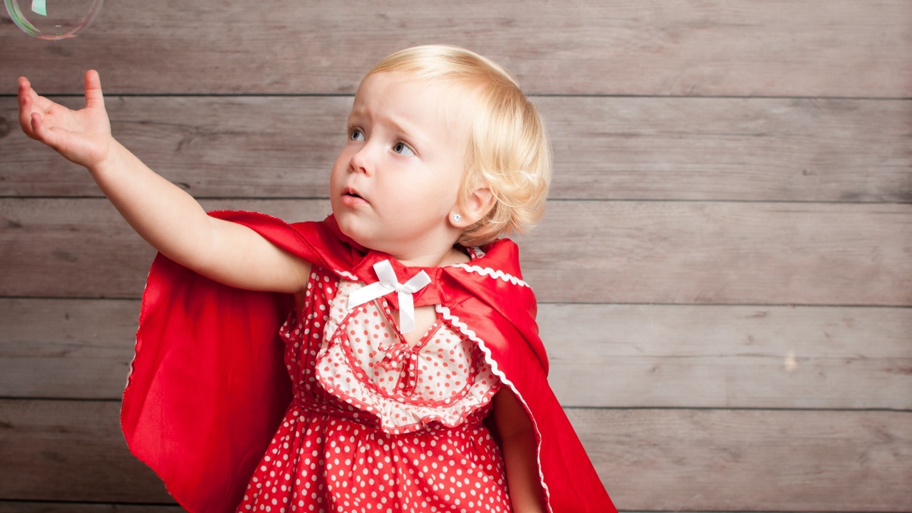 Маленькая девочка в красном платье ловит мыльный пузырь