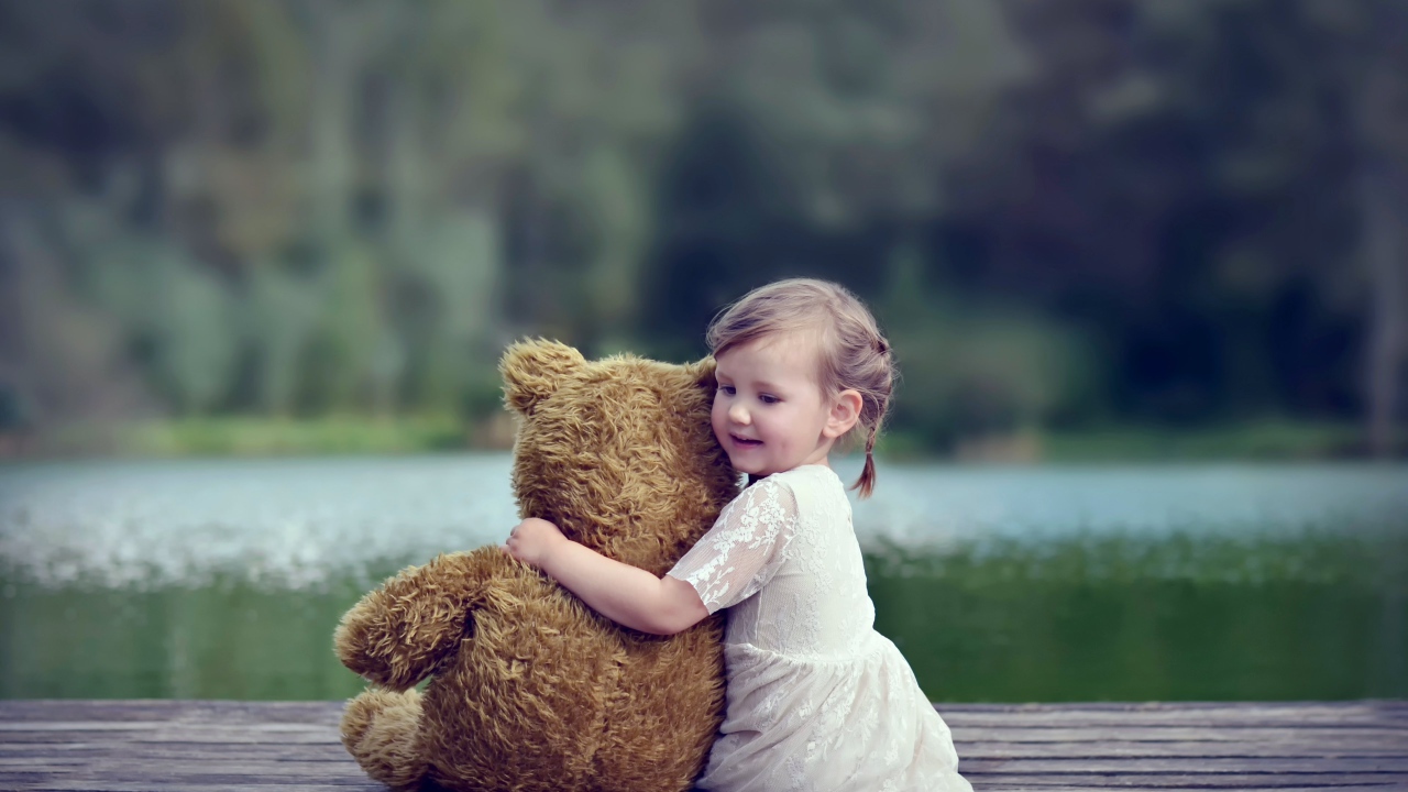 Маленькая девочка в белом платье сидит на мосту с плюшевым медведем