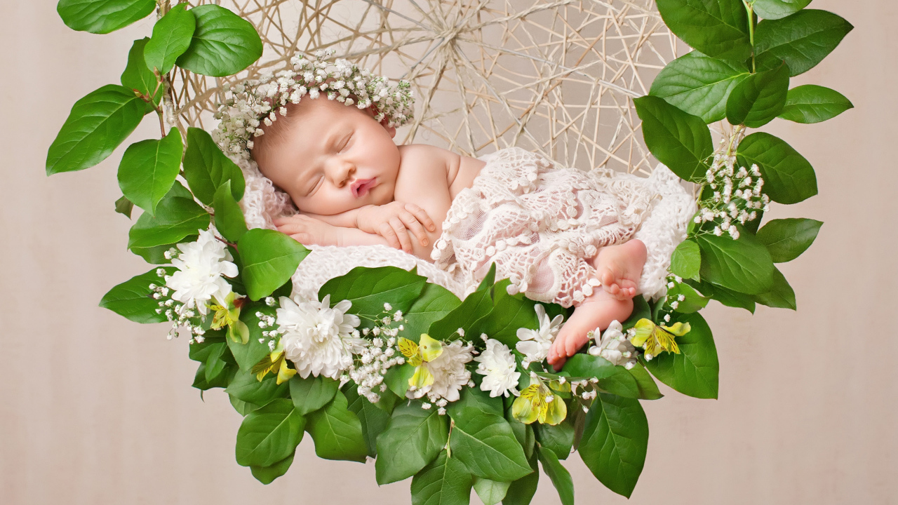 Маленькая девочка спит в колыбеле украшенной зелеными листьями