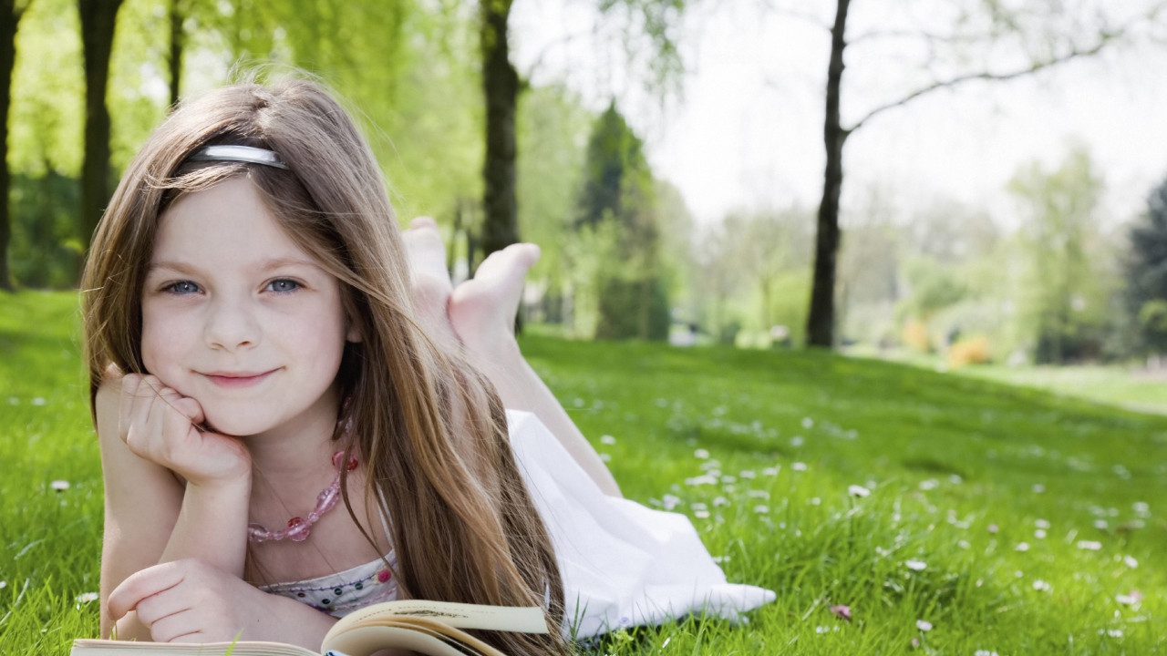 Маленькая девочка с книгой лежит на зеленой траве