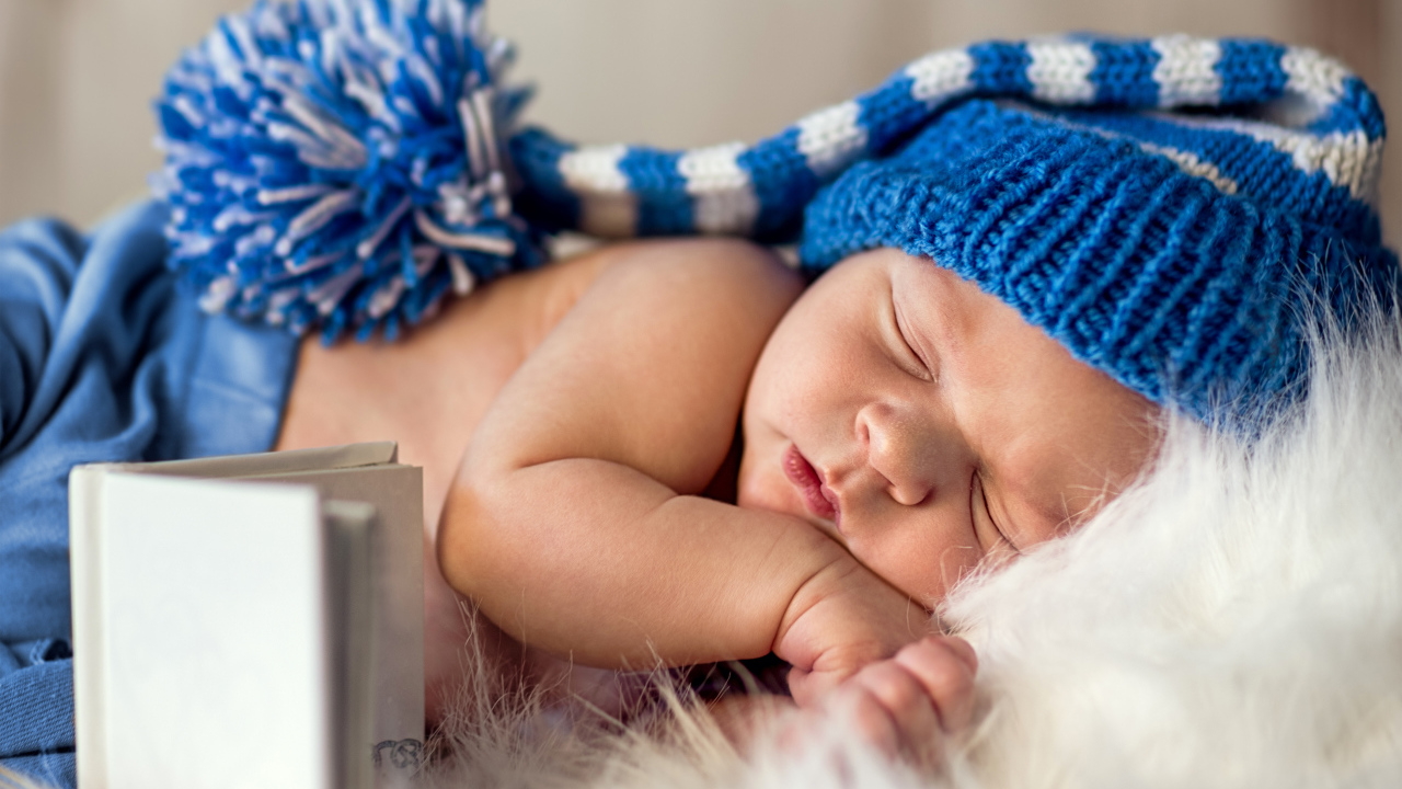 Маленький спящий грудной ребенок в синей вязанной шапке 