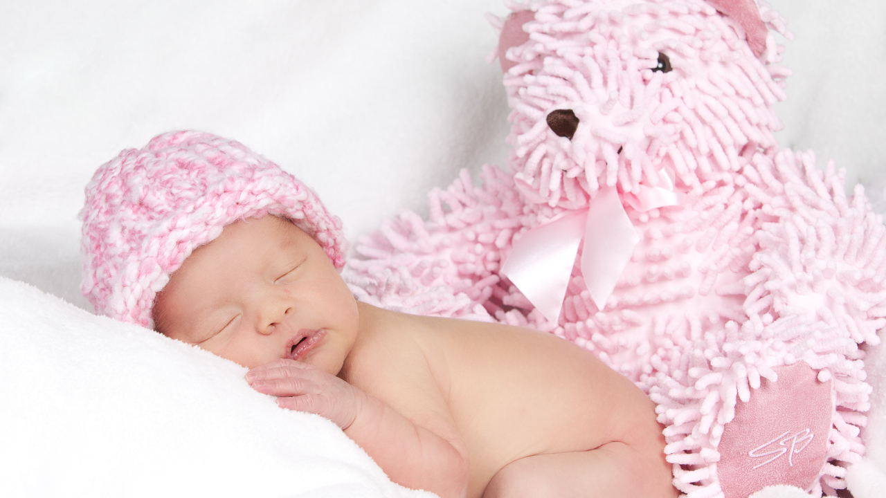 Маленький спящий ребенок в розовой шапке с игрушечным мишкой