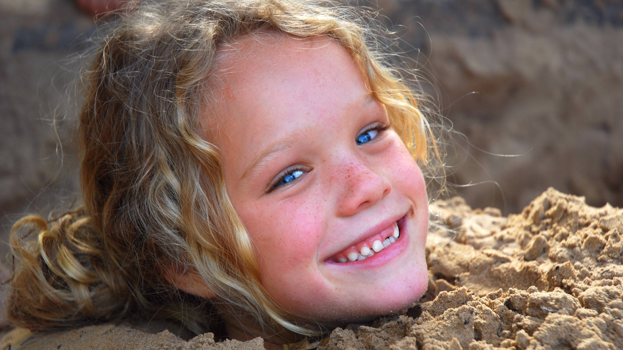 Маленькая улыбающаяся девочка играет в песке