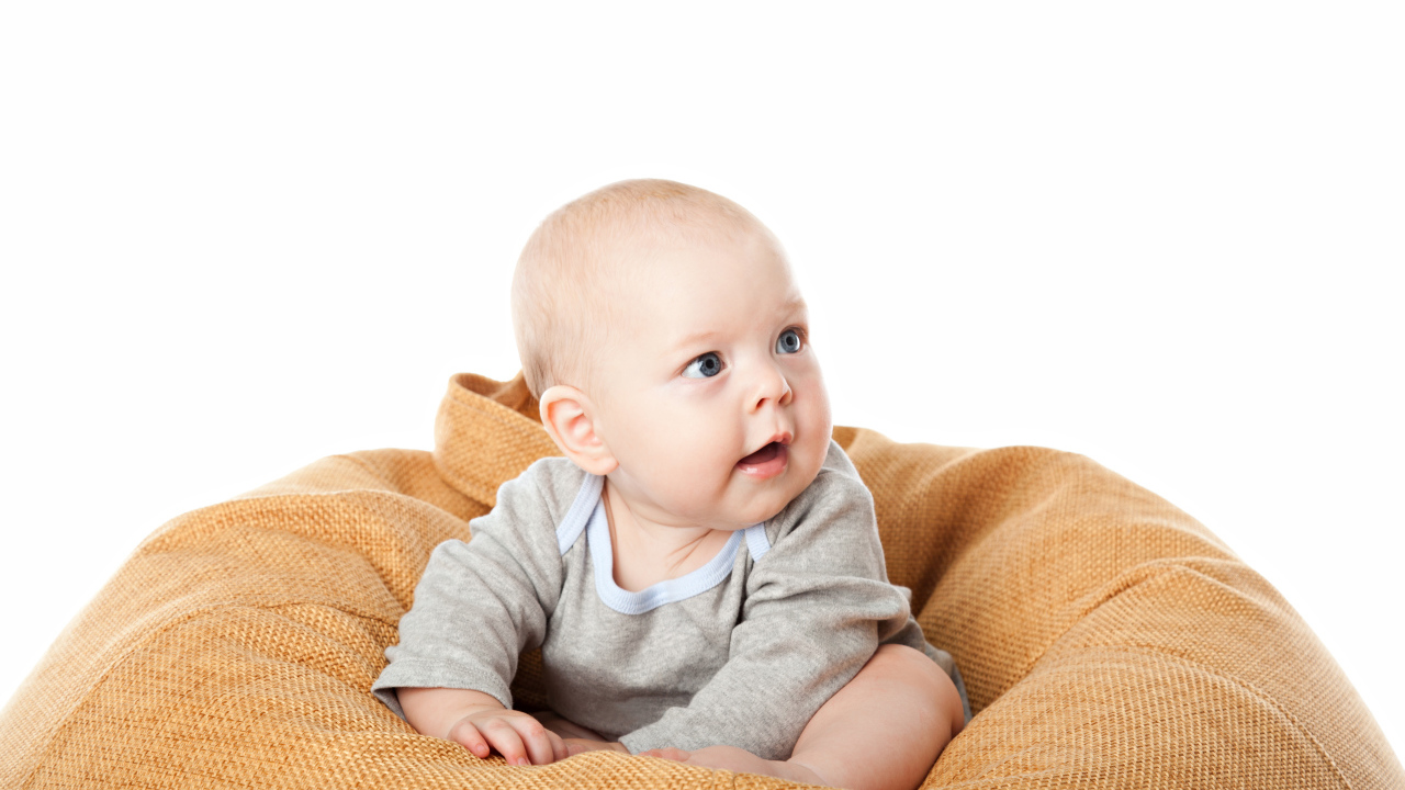 The baby sits on a pillow on a white background
