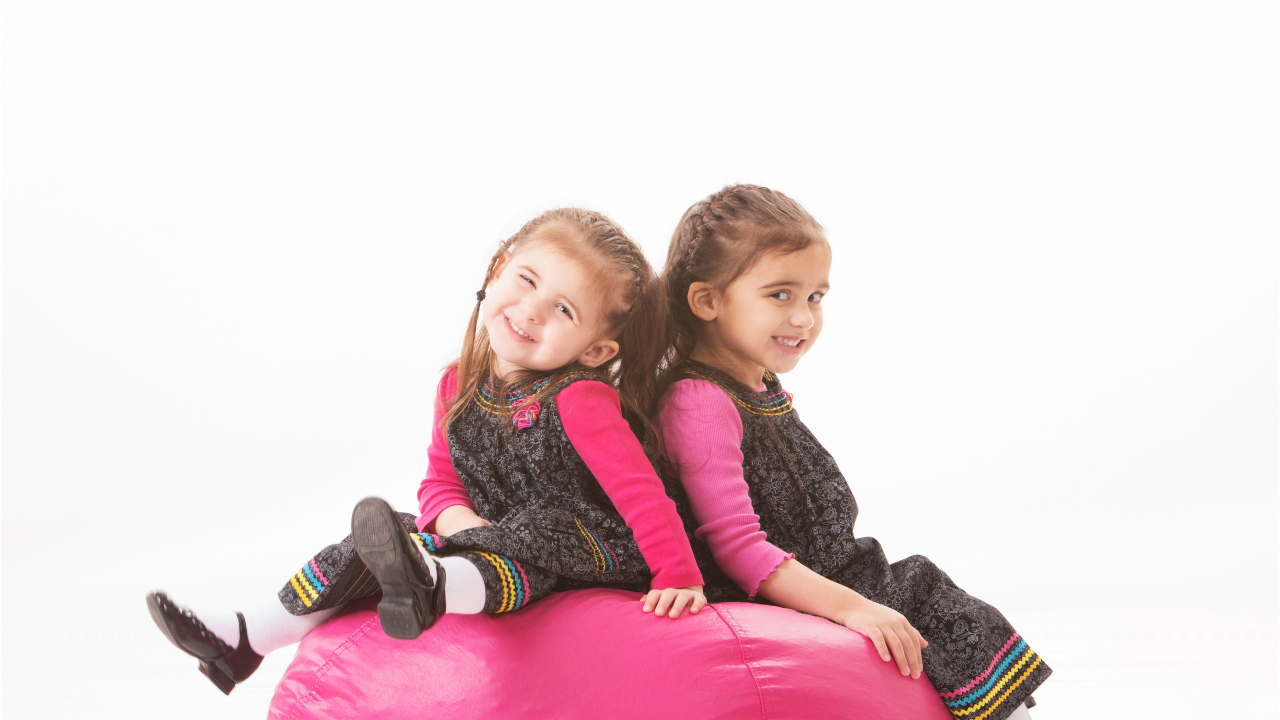 Две маленькие девочки сидят на красном мягком шаре 