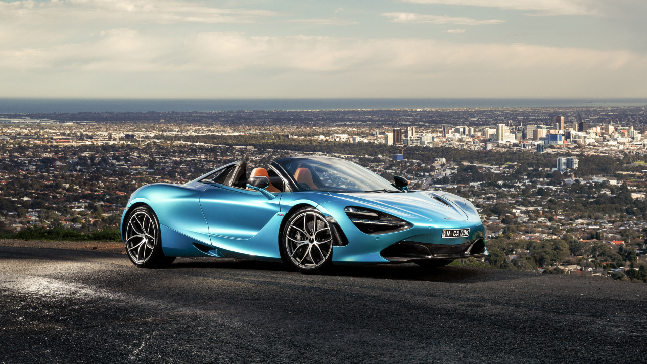 Голубой спортивный автомобиль McLaren 720S Spider 2019 года на фоне города