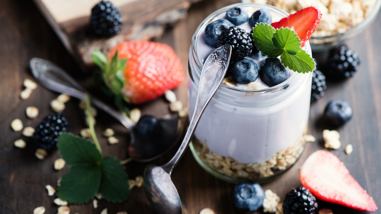 Баночка с мюсли, йогуртом и ягодами на столе с ложками