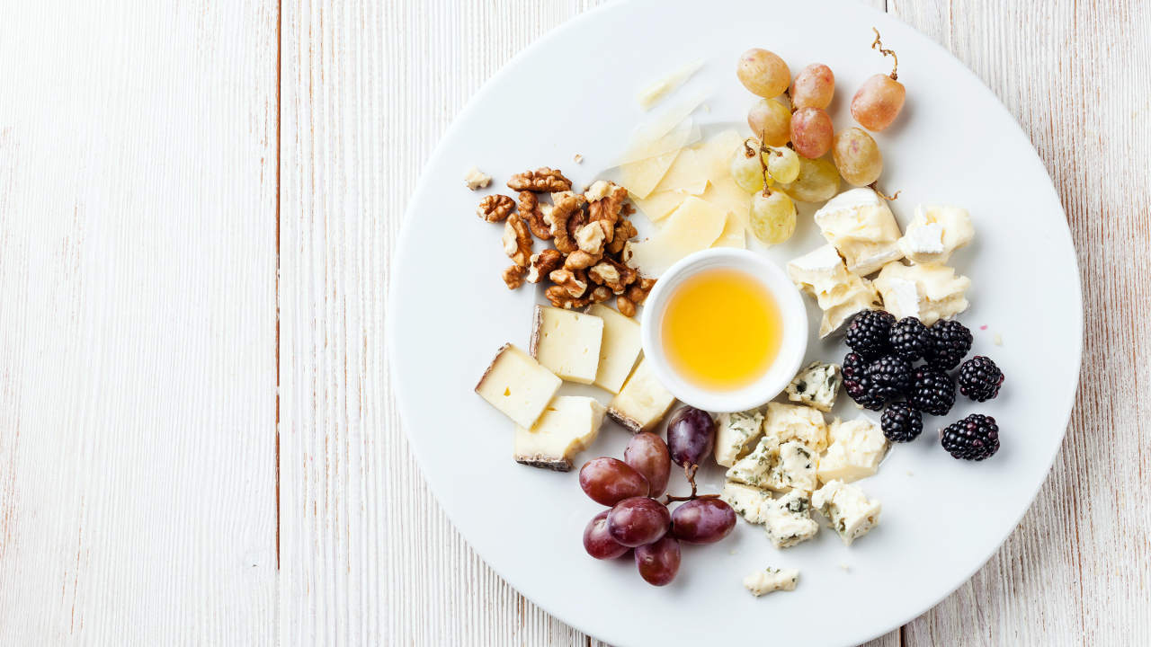 Куски сыра на тарелке с орехами, виноградом, медом и ягодами ежевики