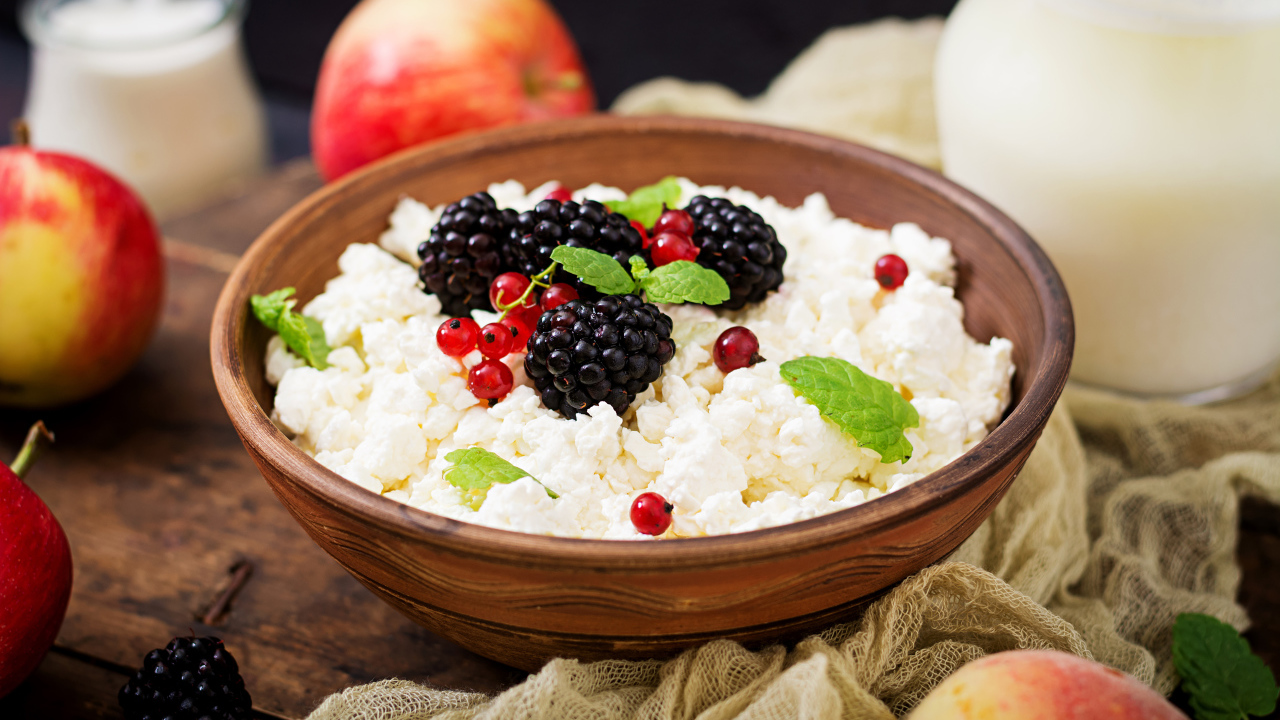 Творог с ягодами в деревянной миске на столе с яблоками