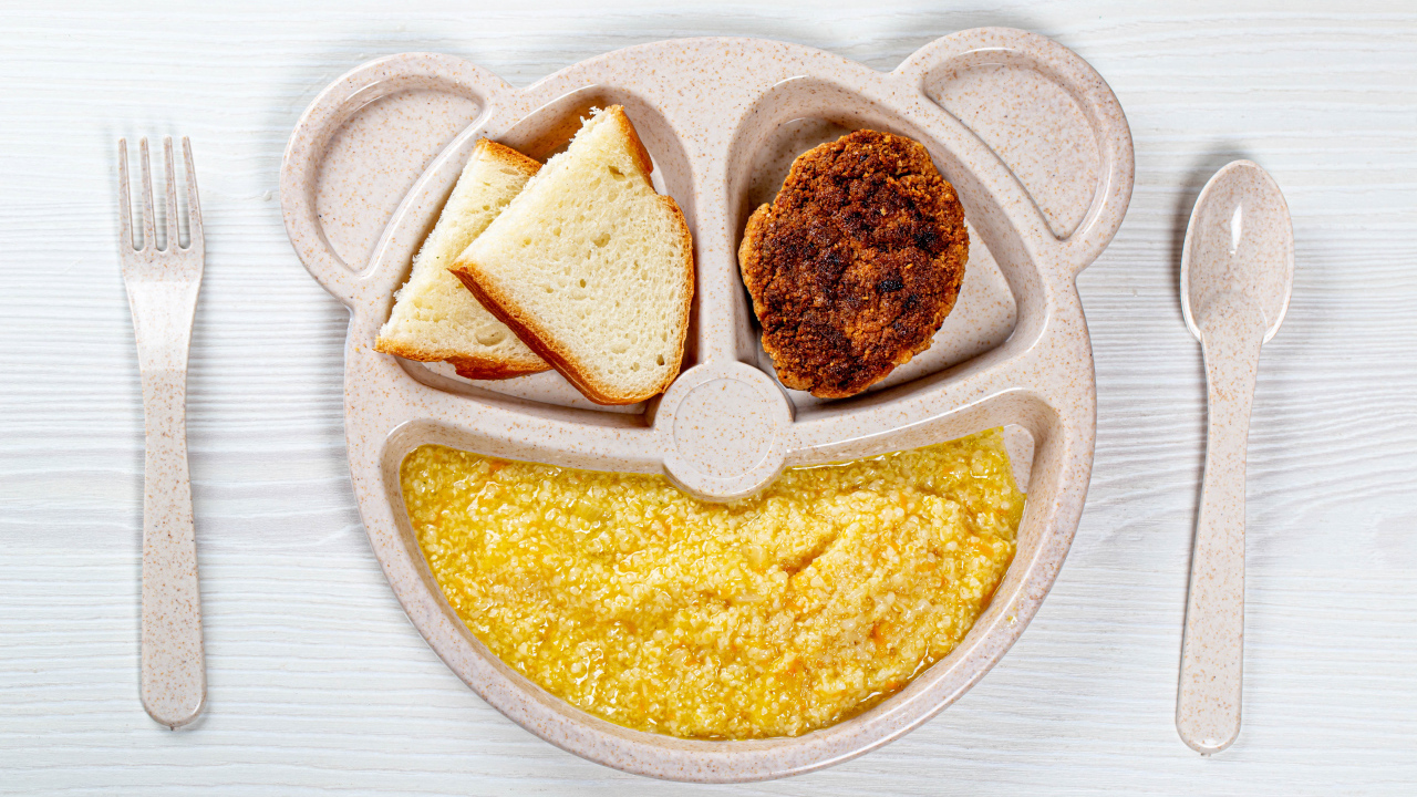 Каша на тарелке с котлетой и хлебом для ребенка