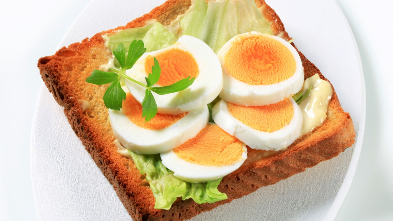 Тост с листом салата и кусочками яйца на белой тарелке 