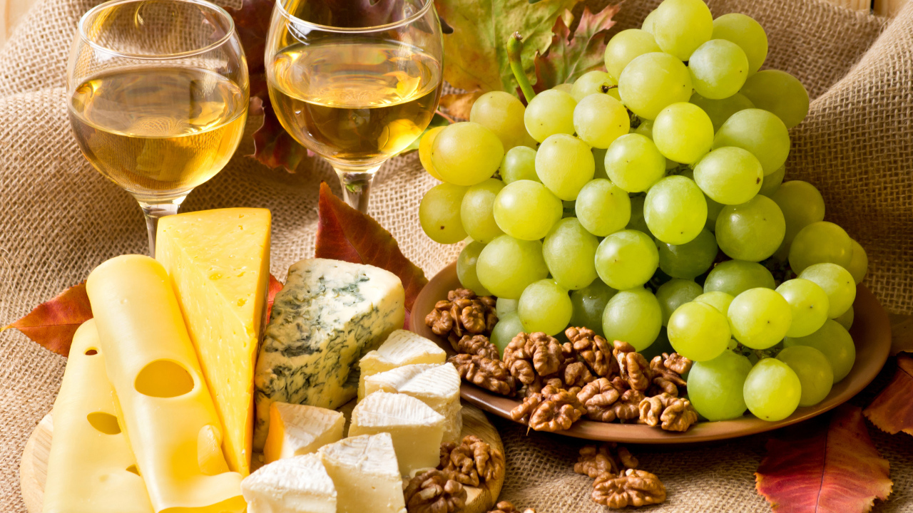Белое вино на столе с сыром, виноградом и орехами