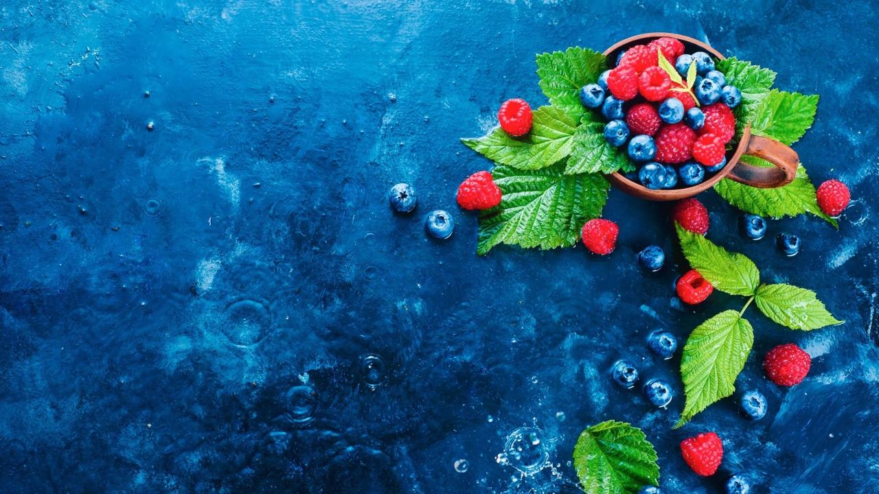 Чашка с ягодами черники и малины на синем столе