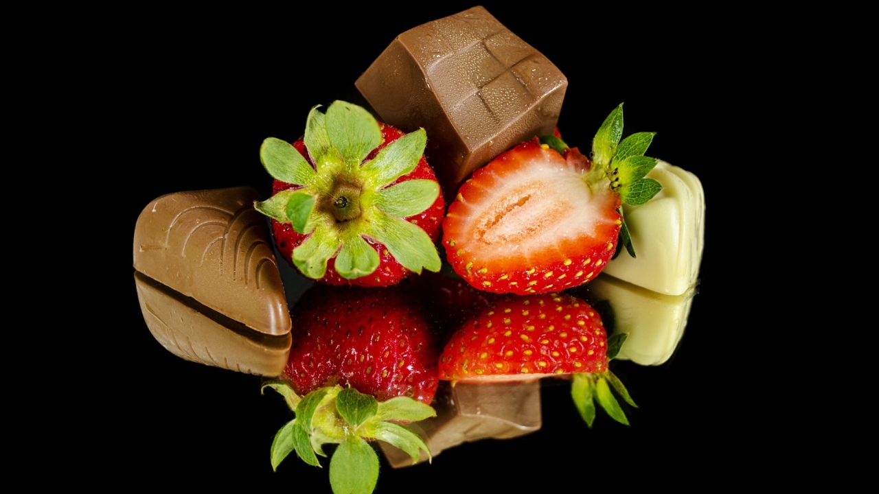 Красная свежая клубника с шоколадными конфетами на черном фоне