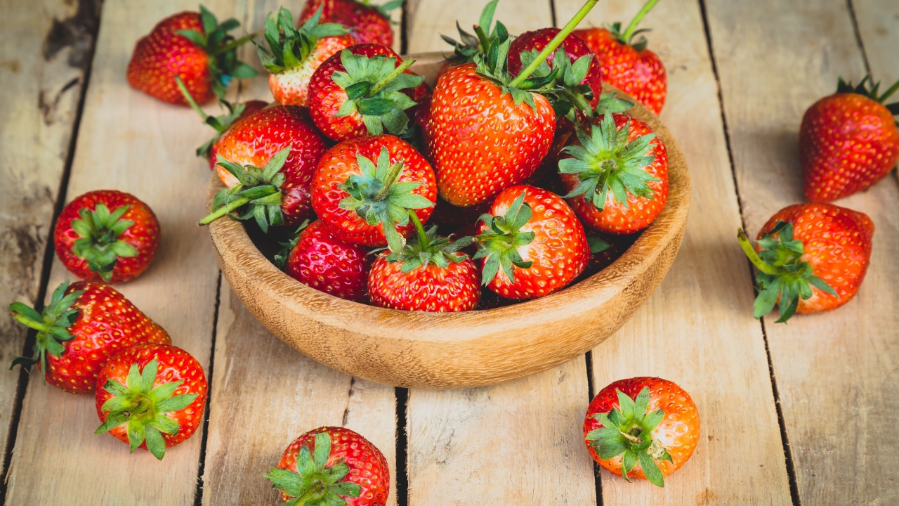 Спелая красная клубника в деревянной миске на столе