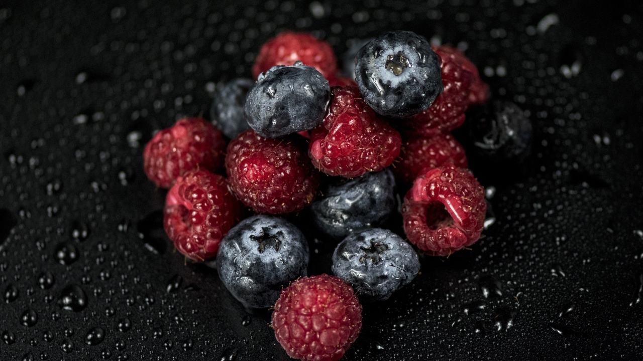 Мокрые ягоды черники и малины на черном фоне