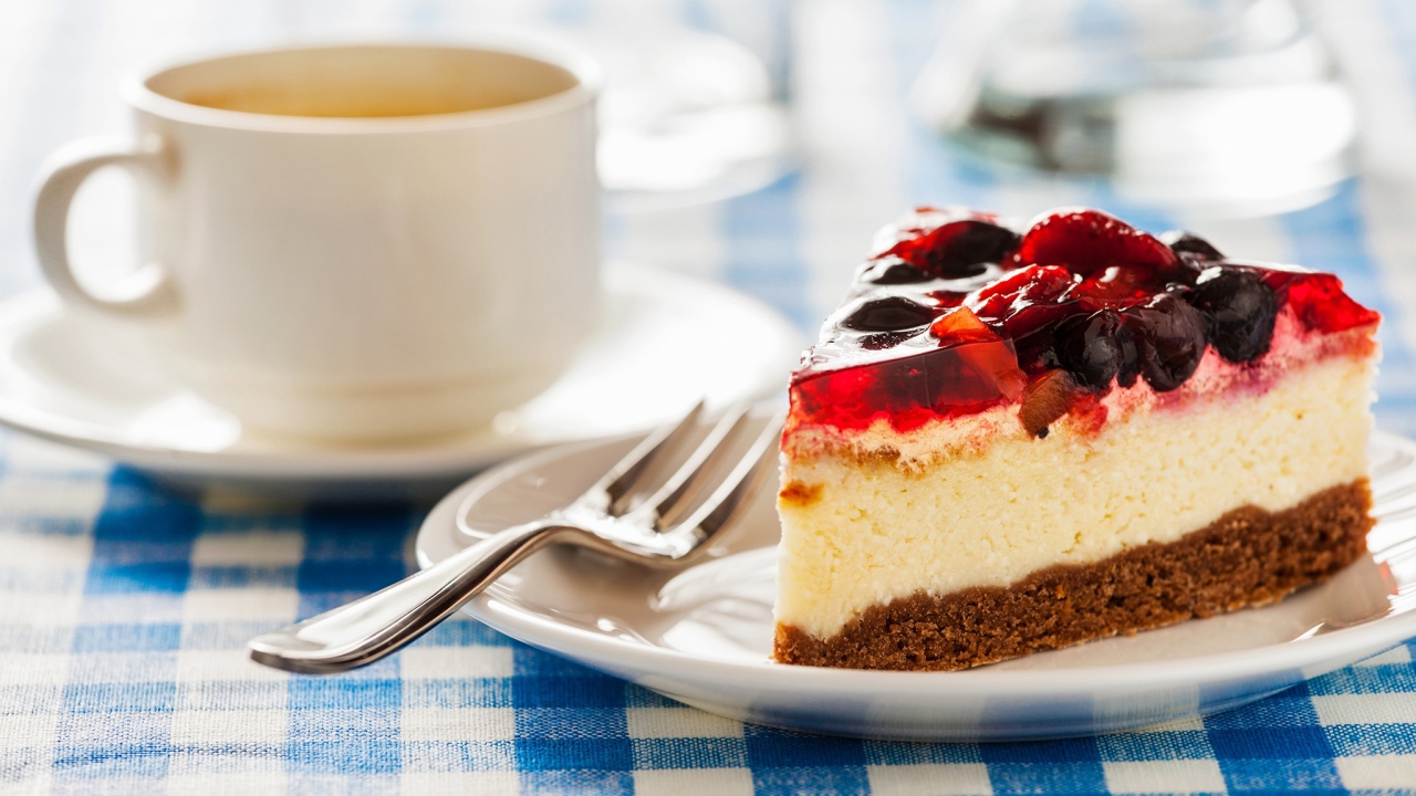 Кусок чизкейка с ягодами и желе на столе с чашкой кофе