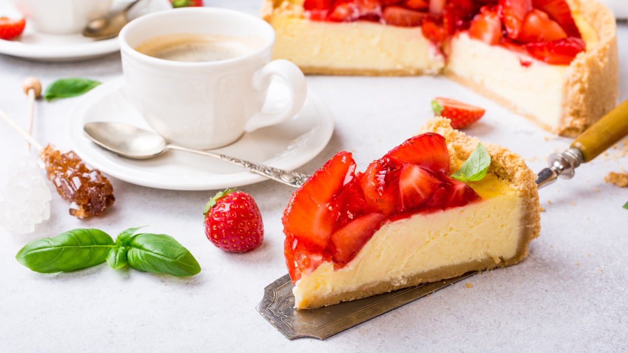 Кусок чизкейка с клубникой на столе с кофе