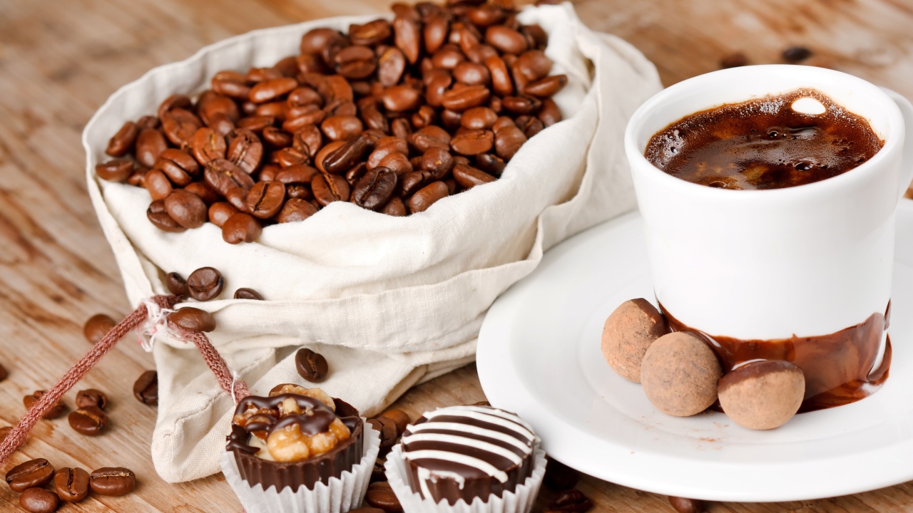 Шоколадные конфеты на столе с чашкой кофе и мешком с кофейными зернами