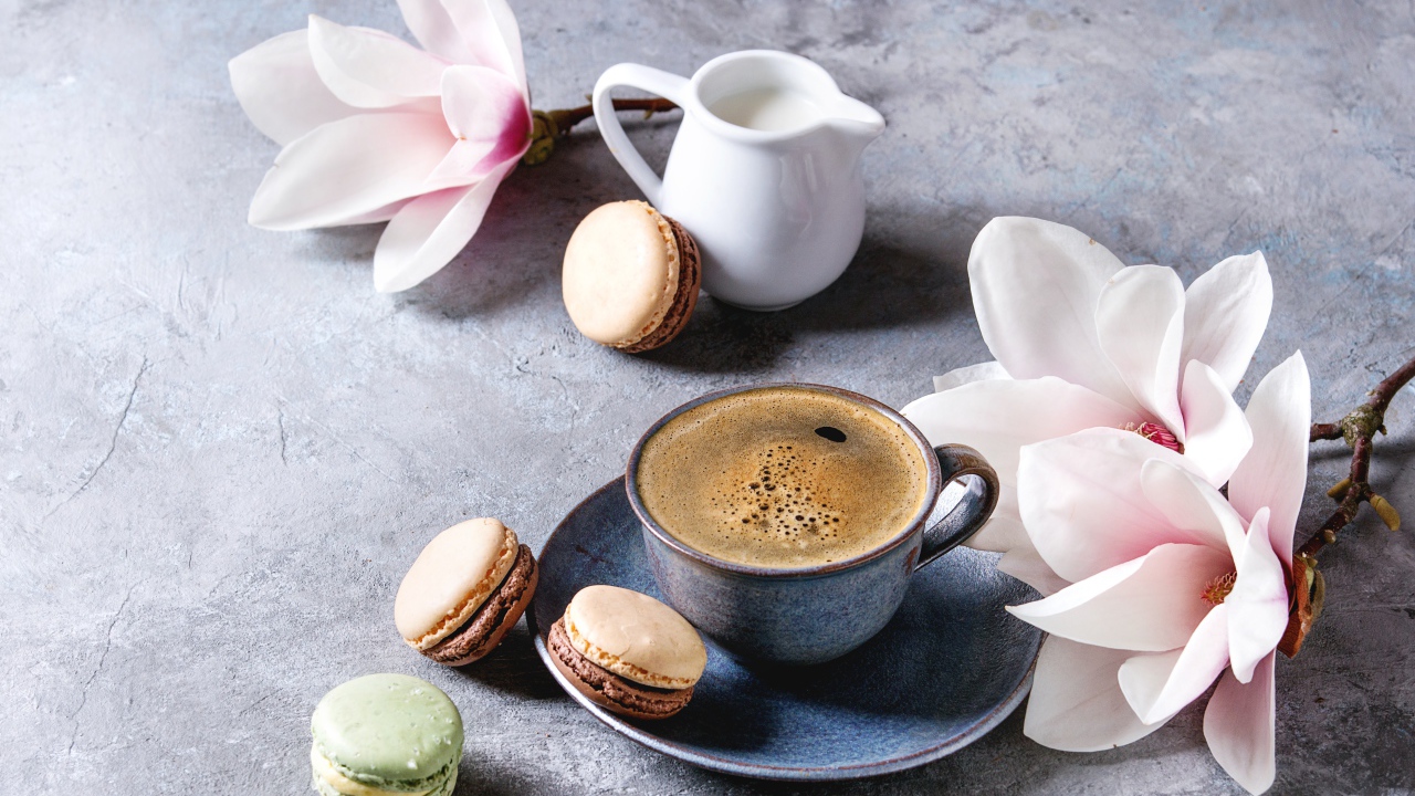 Кофе на столе с макарунами, молоком и цветами 