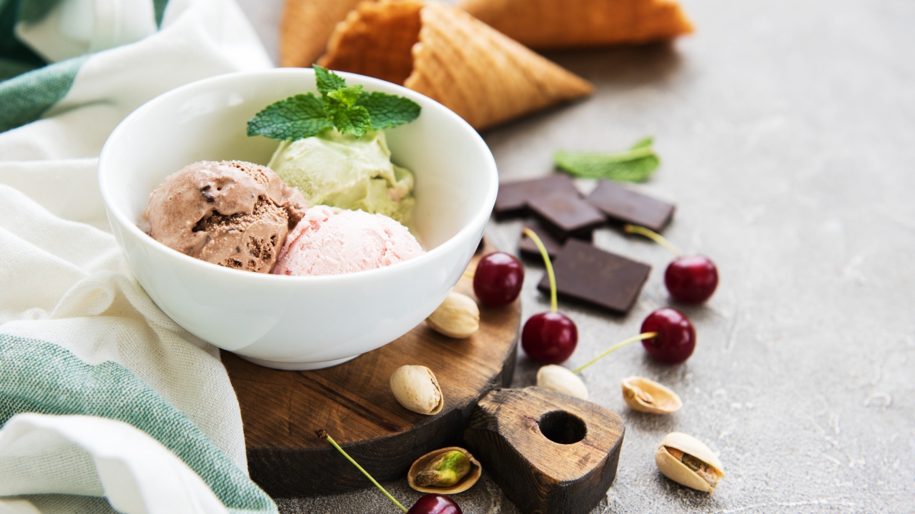 Шарики мороженого на столе вафельными рожками, черешней и фисташками