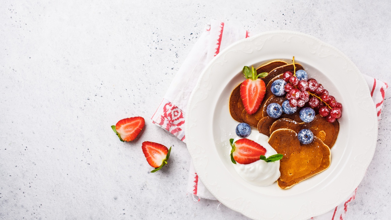 Оладьи со сметаной в тарелке с ягодами черники, клубники и красной смородины