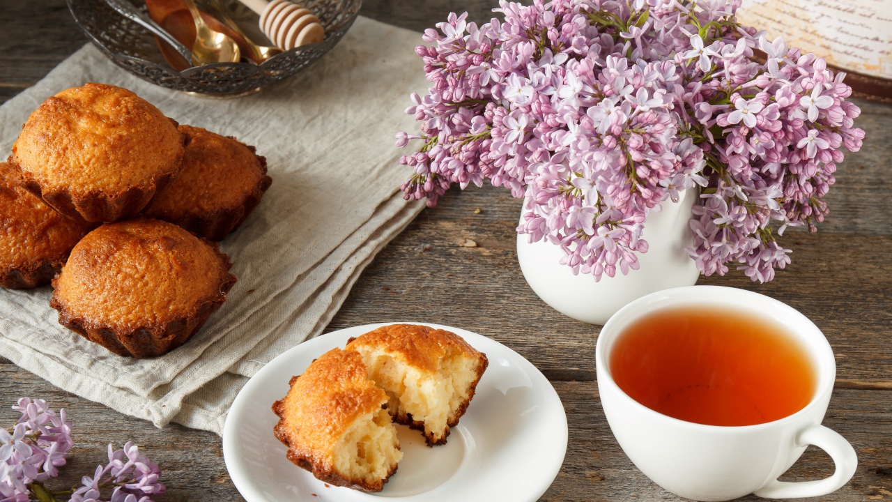 Сладкие кексы на столе с чаем и букетом сирени