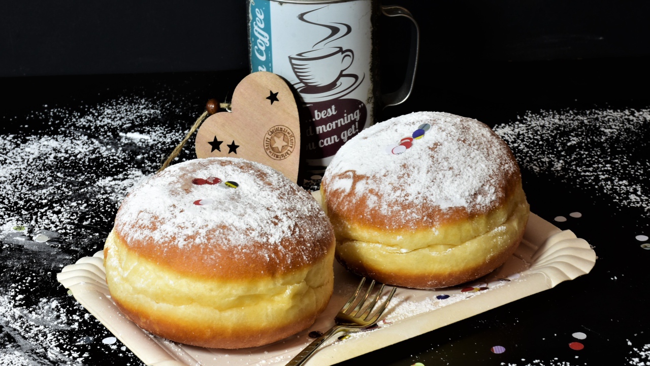 Два пышных пончика с сахарной пудрой на черном столе с кофе
