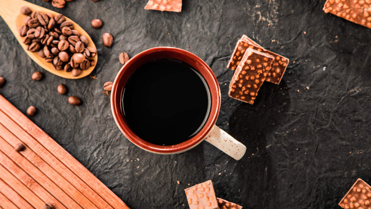 Чашка кофе на столе с кусочками шоколада и кофейными зернами