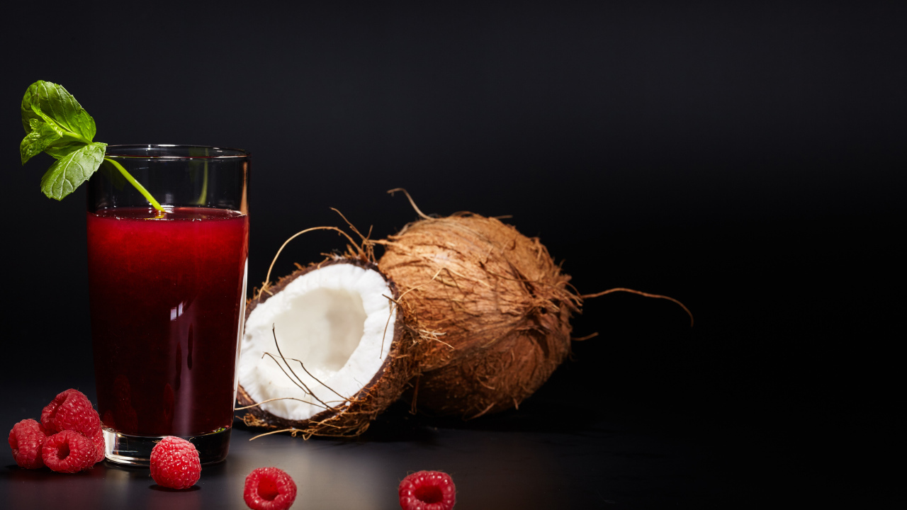 Стакан сока на столе с кокосом и ягодами малины 