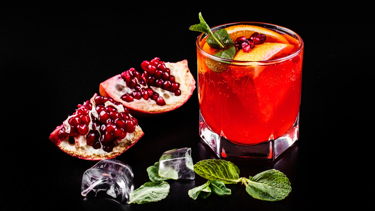 Алкогольный напиток в стакане на черном фоне с гранатом, кусочками льда и мятой