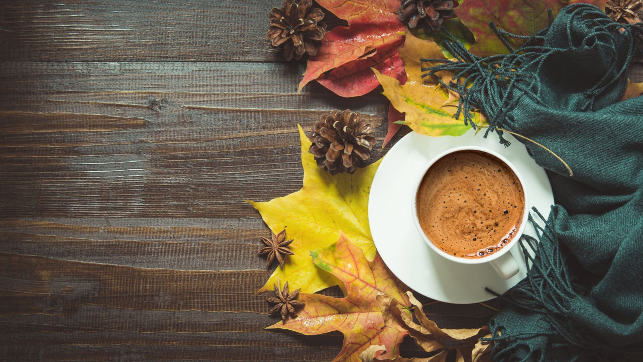 Чашка кофе на столе с шарфом, желтыми листьями и шишками