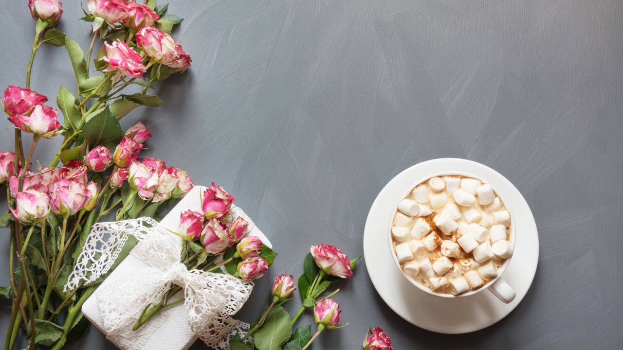 Чашка кофе с маршмеллоу на столе с подарком и букетом роз