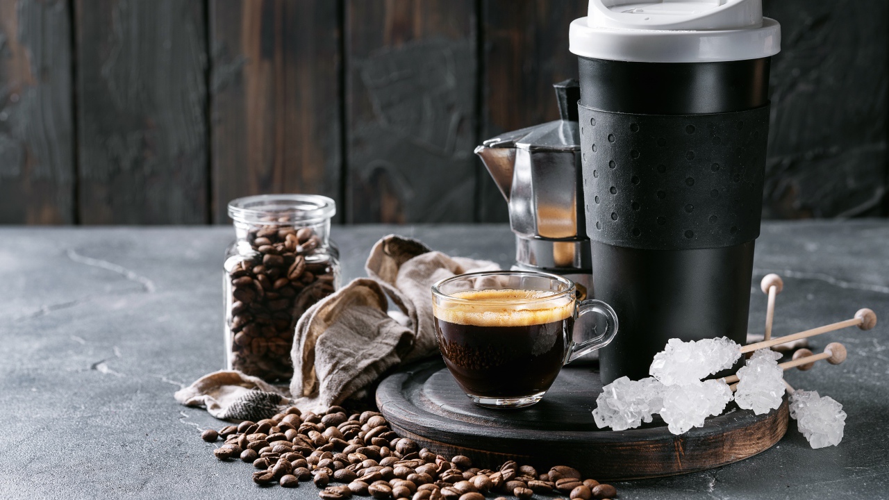 Стеклянная чашка кофе на столе с термосом и зернами