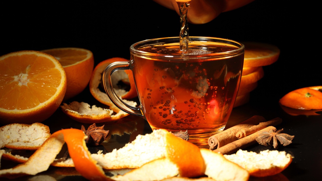 Стеклянная чашка с чаем на столе с апельсинами и корицей