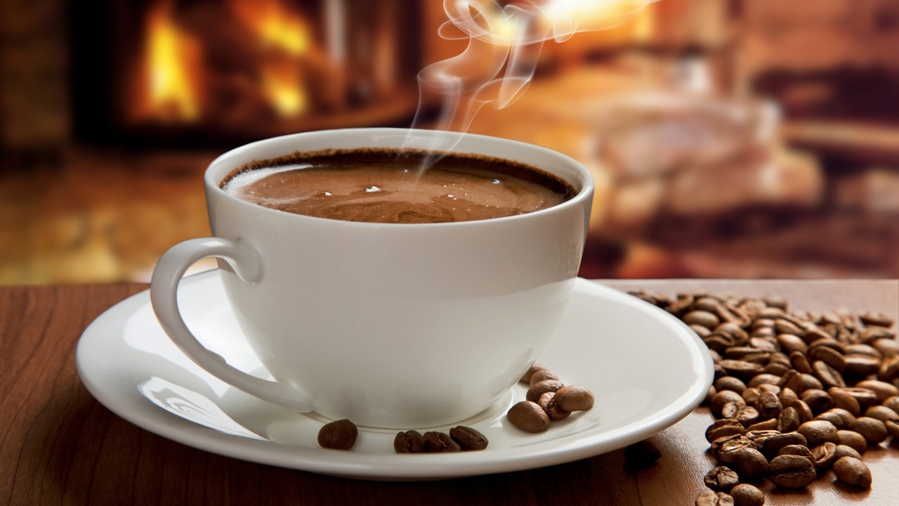 Большая белая чашка с горячим кофе на столе с кофейными зернами