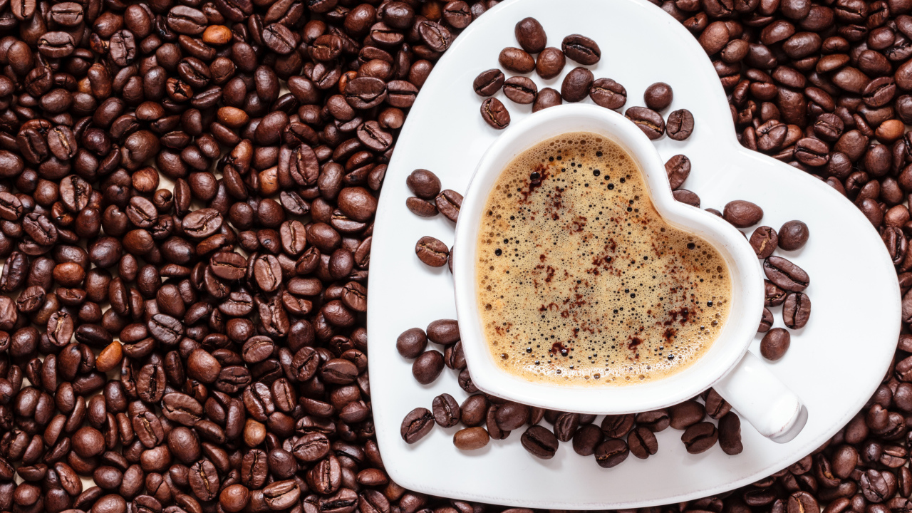 Белая чашка в форме сердца стоит на кофейных зернах 