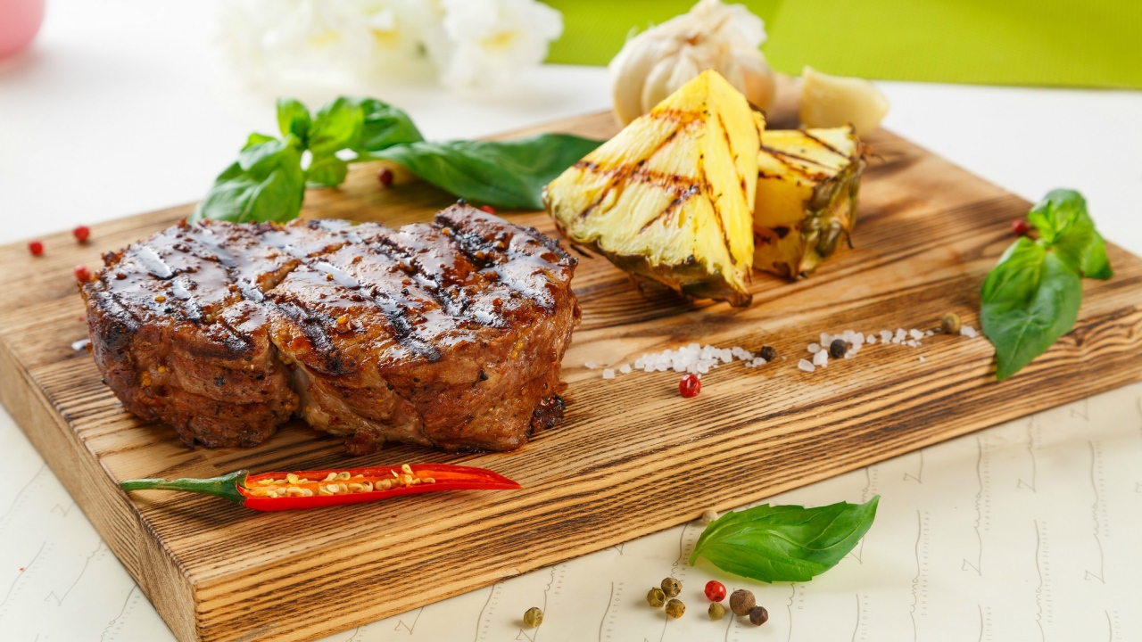 Кусок мяса гриль на деревянной доске с кусочками ананаса и базиликом