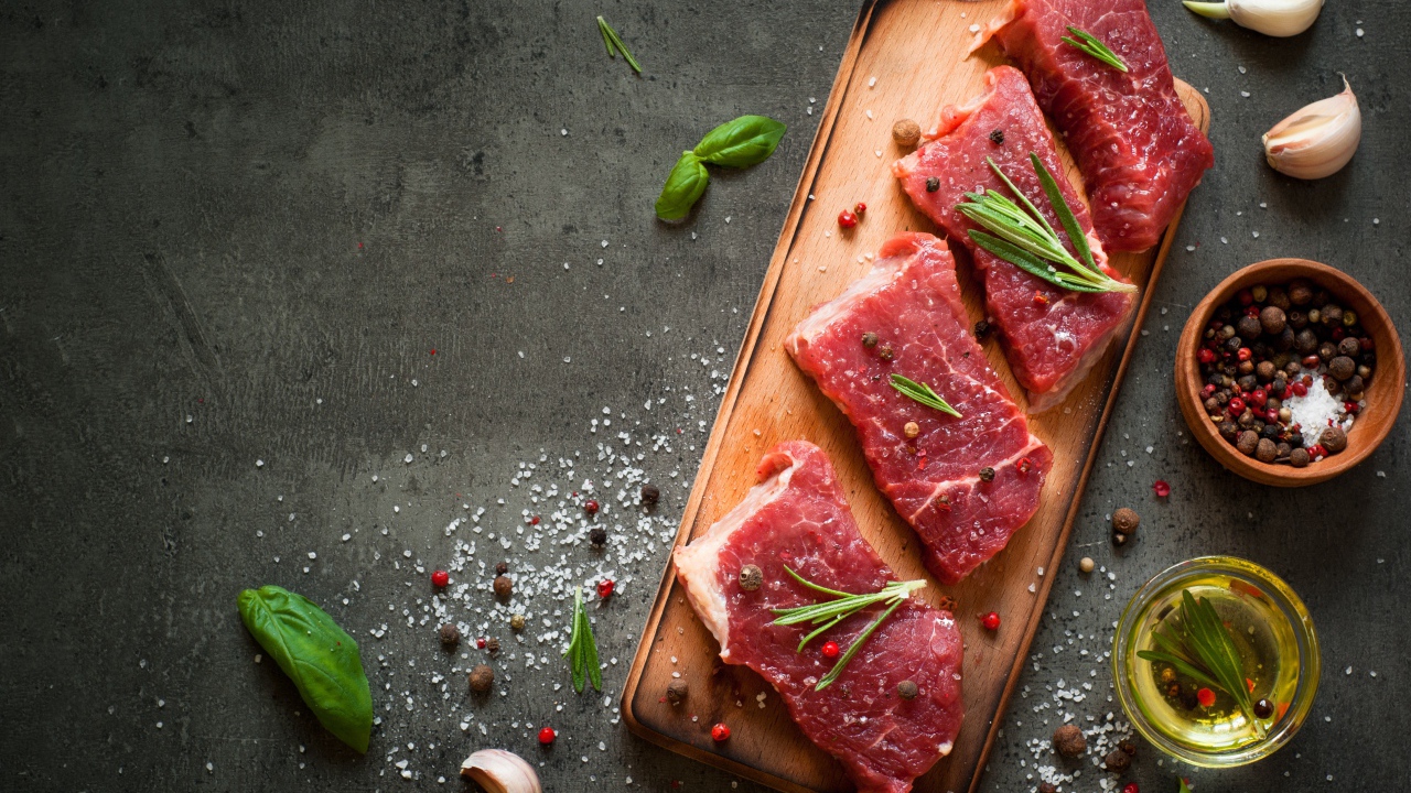 Куски мяса на разделочной доске с зеленью и специями