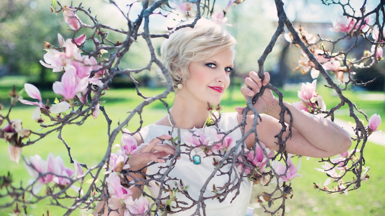 Красивая женщина с короткой стрижкой стоит у цветущей магнолии 