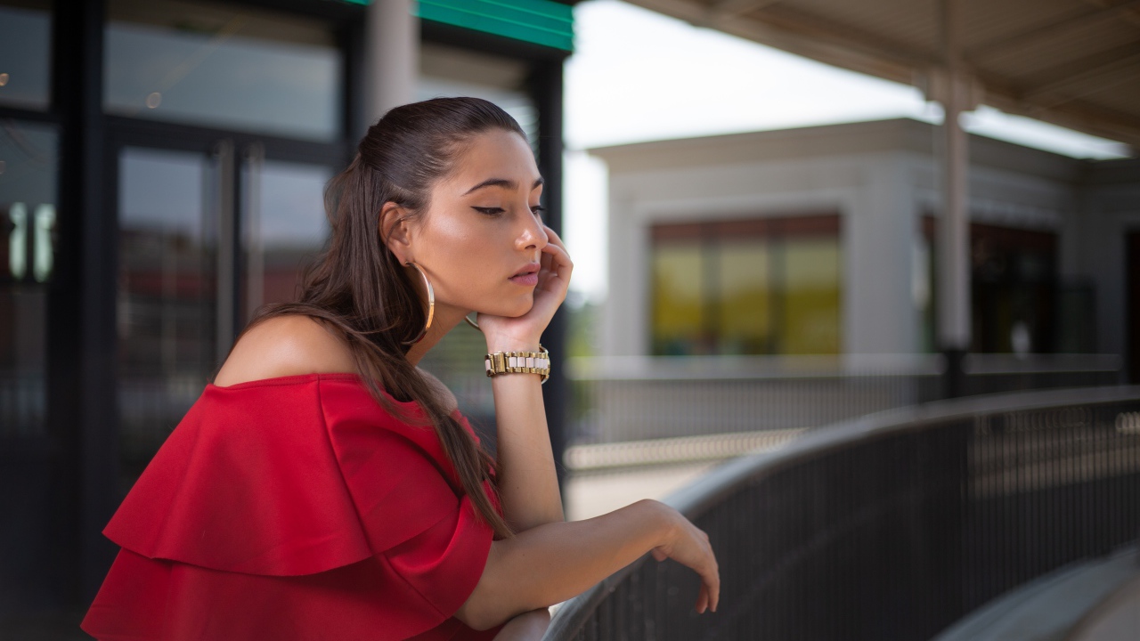 Задуманная девушка в красном платье стоит у перил 