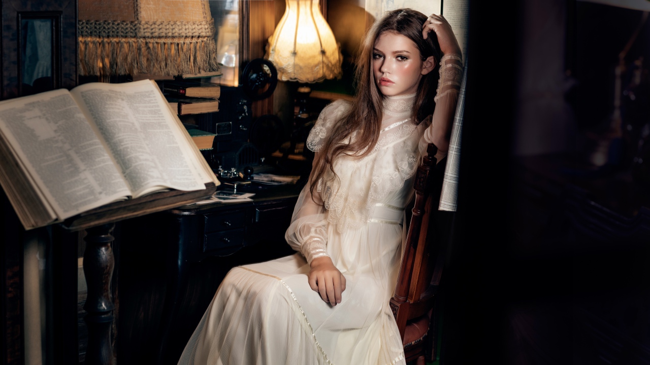 Девушка в красивом белом платье сидит на стуле у стола