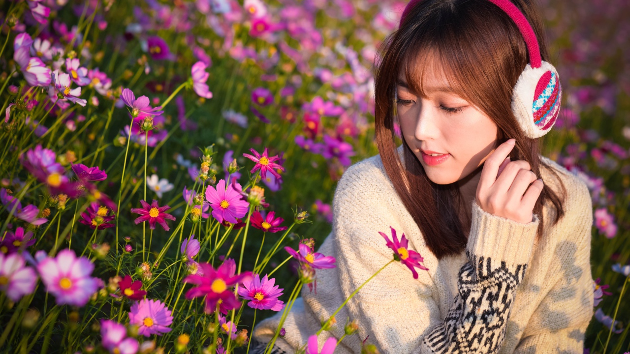 Девушка азиатка в наушниках сидит в цветах космеи