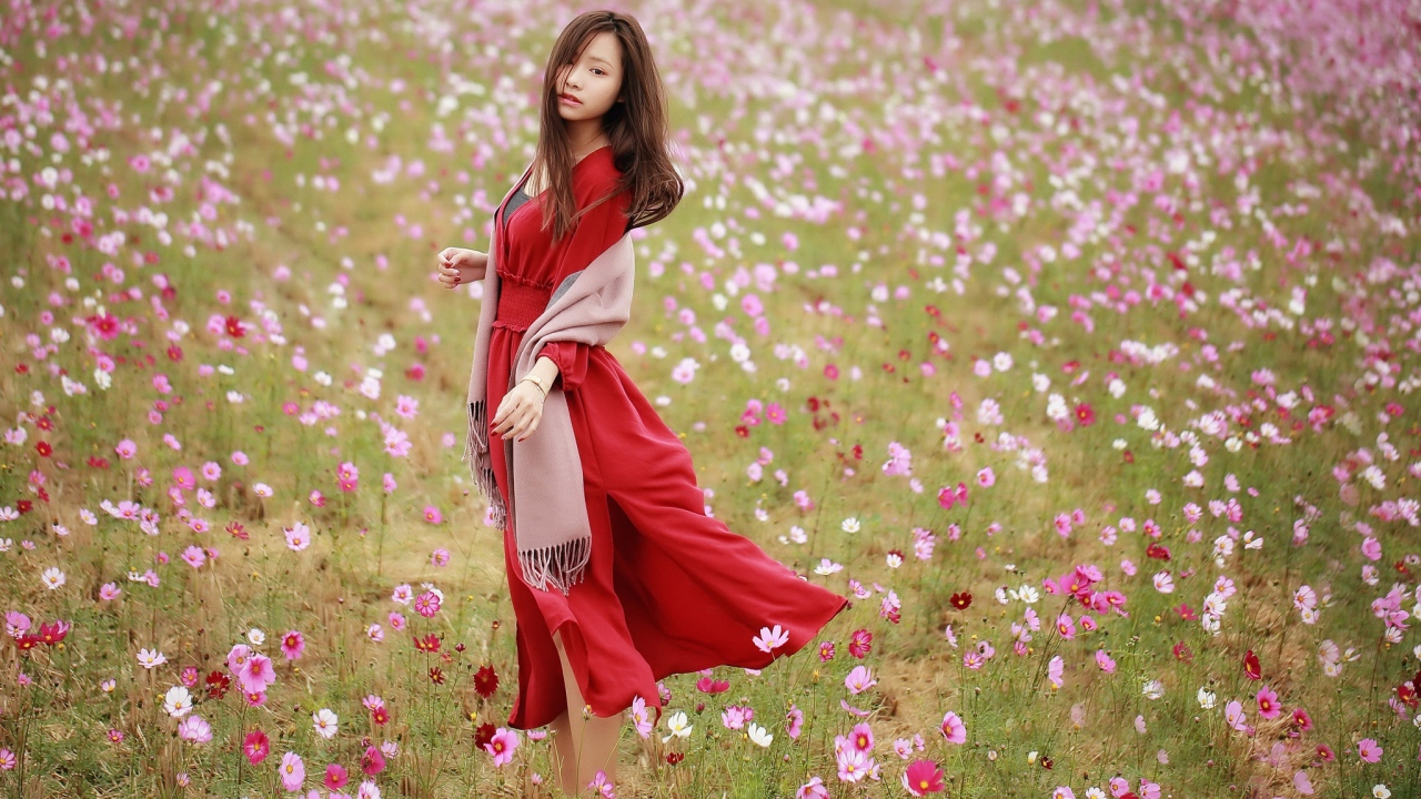 Красивая азиатка в красном платье на поле с цветами космеи