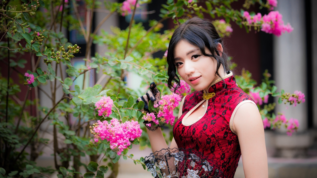 Красивая азиатка с веером в руках стоит у куста с розовыми цветами
