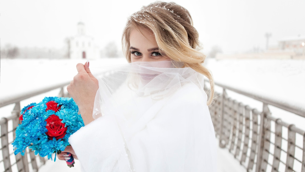 Красивая невеста с букетом в руках закрывает лицо фатой