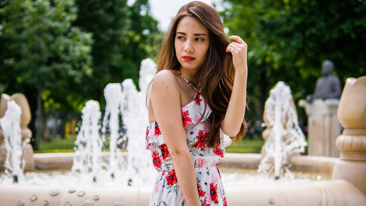 Красивая шатенка в цветастом платье у фонтана летом