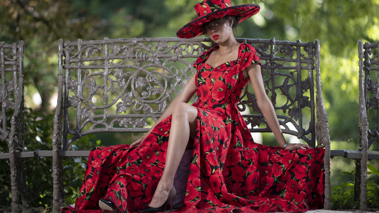 Красивая темнокожая девушка в красном платье сидит на лавке